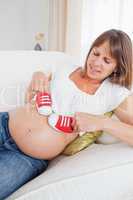 Charming pregnant woman playing with red baby shoes while lying