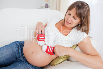Beautiful pregnant woman playing with red baby shoes while lying