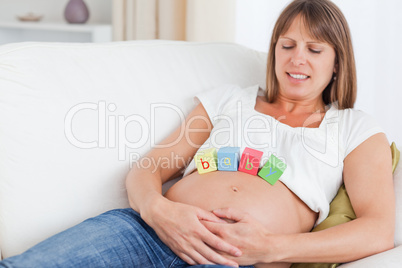 Beautiful pregnant woman playing with wooden blocks while lying