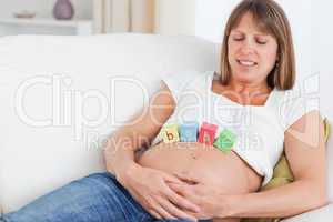 Beautiful pregnant woman playing with wooden blocks while lying