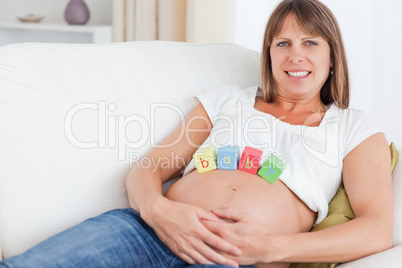 Pretty pregnant woman playing with wooden blocks while lying on