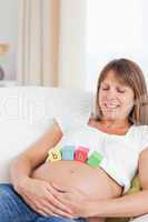 Charming pregnant woman playing with wooden blocks while lying o