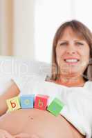 Good looking pregnant woman playing with wooden blocks while lyi
