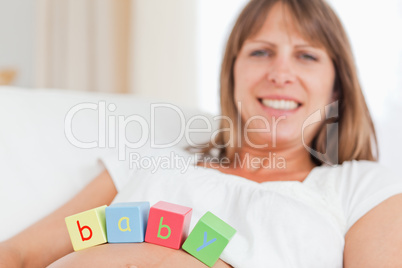 Cute pregnant woman playing with wooden blocks while lying on a