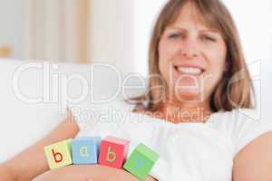 Cute pregnant woman playing with wooden blocks while lying on a