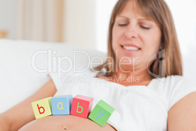 Gorgeous pregnant woman playing with wooden blocks while lying o