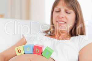 Gorgeous pregnant woman playing with wooden blocks while lying o