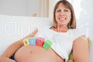 Pretty pregnant female playing with wooden blocks while lying on