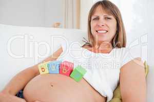 Lovely pregnant female playing with wooden blocks while lying on