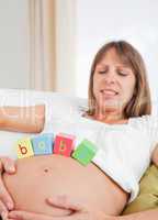 Beautiful pregnant female playing with wooden blocks while lying