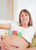 Good looking pregnant female playing with wooden blocks while ly