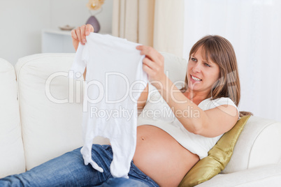 Beautiful pregnant woman holding a baby grow while lying on a so