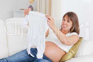 Beautiful pregnant woman holding a baby grow while lying on a so