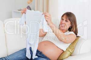 Pretty pregnant woman holding a baby grow while lying on a sofa