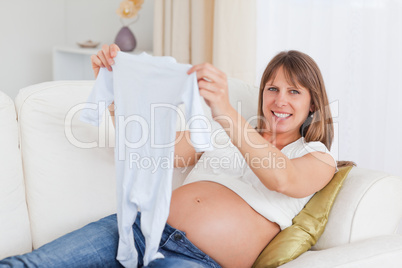 Charming pregnant woman holding a baby grow while lying on a sof