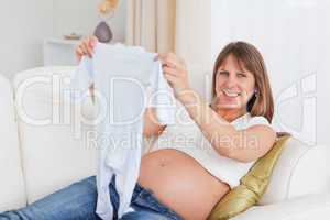 Charming pregnant woman holding a baby grow while lying on a sof