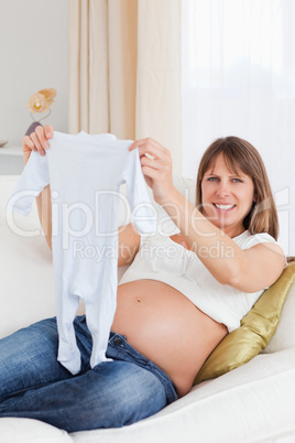 Gorgeous pregnant woman holding a baby grow while lying on a sof