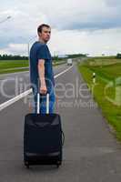 The young man pending on road with a suitcase