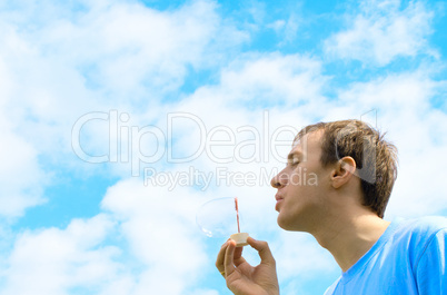 The young man starts up soap bubbles against the blue sky