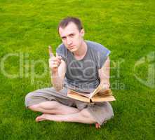 A young man reading a book on the grass