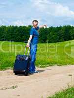 The young man on road in the field with a suitcase