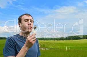 The young man blows on a dandelion on a green meadow