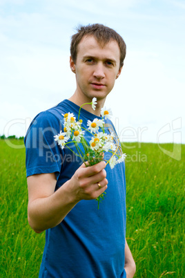 The young man with camomiles on a green meadow