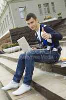 Young student working on a laptop. Thumb up