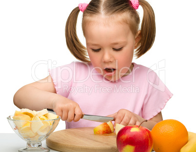 Little girl is cutting fruits for salad