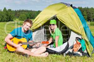 Camping couple playing guitar by tent countryside