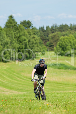 Sportive man mountain biking uphill sunny meadows