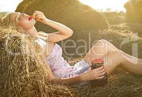 beautiful woman sitting on the hay with a pitcher of raspberry