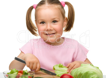 Little girl is cutting carrot for salad