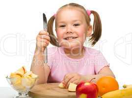 Little girl is cutting fruits for salad