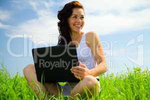 Cute girl is sitting on green grass with laptop