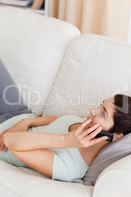 Portrait of a calm brunette calling while lying on a sofa