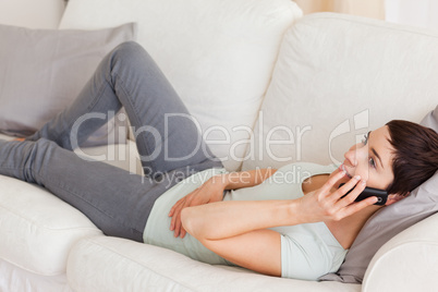 Calm brunette calling while lying on a sofa