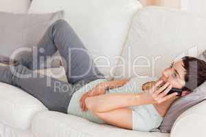 Calm brunette calling while lying on a sofa
