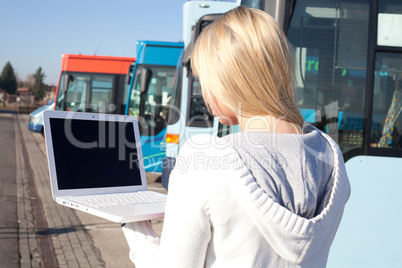 young blond woman with laptop in front of busses