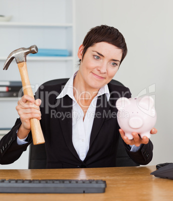 Smiling office worker breaking a piggybank with a hammer
