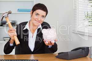 Cute office worker breaking a piggybank with a hammer