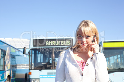 young blond woman with a cell phone in front of a bus