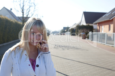 young blond woman with a cell phone on a village street