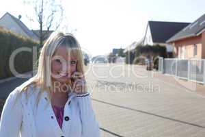 young blond woman with a cell phone on a village street