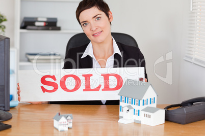 Female real estate agent with a sold panel and houses miniatures