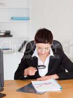 Portrait of a woman looking at a chart with a magnifying glass in her office