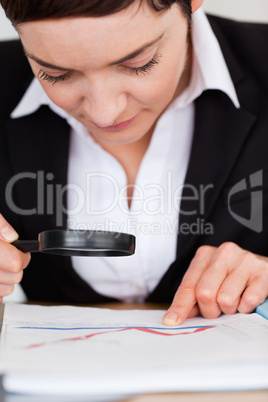 Businesswoman looking at a chart with a magnifying glass in her office