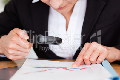 Feminine hands holding a magnifying glass above a chart