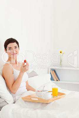 Portrait of a smiling brunette eating a strawberry