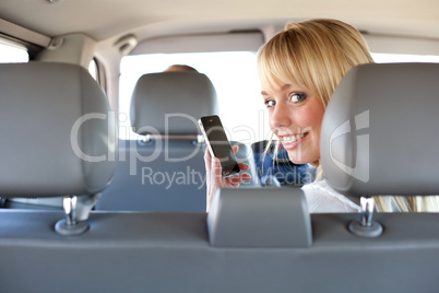 young blond woman with a smartphone on a backseat of a car